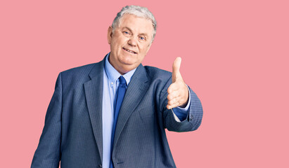 Senior grey-haired man wearing business jacket smiling friendly offering handshake as greeting and welcoming. successful business.