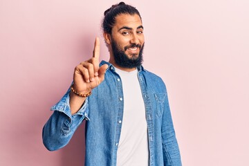 Young arab man wearing casual clothes smiling with an idea or question pointing finger up with happy face, number one