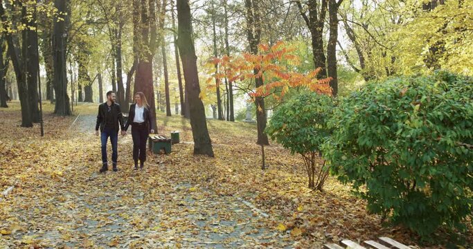 Couple walking in autumn park, rejoicing while embracing and kissing each other