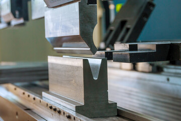 Bending sheet metal on a hydraulic machine at the factory. Bend tools, press brake punch and die. Close-up.