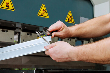 The worker measures the product after bending on a hydraulic press for bending sheet metal.