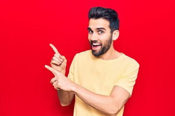 Young handsome man with beard wearing casual t-shirt smiling and looking at the camera pointing with two hands and fingers to the side.