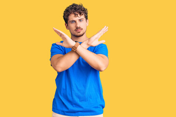 Young handsome man with curly hair wearing casual clothes rejection expression crossing arms doing...