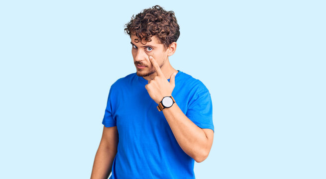 Young handsome man with curly hair wearing casual clothes pointing to the eye watching you gesture, suspicious expression