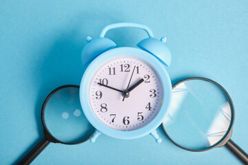 magnifiers and light blue alarm clock on a blue background