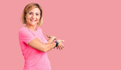Young blonde woman wearing sportswear inviting to enter smiling natural with open hand