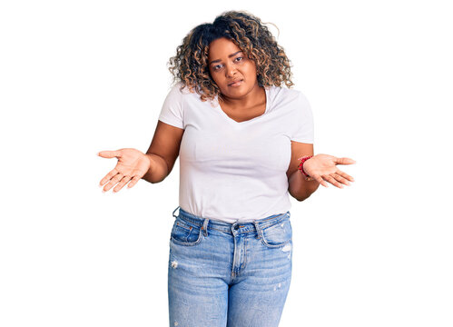 Young african american plus size woman wearing casual clothes clueless and confused expression with arms and hands raised. doubt concept.