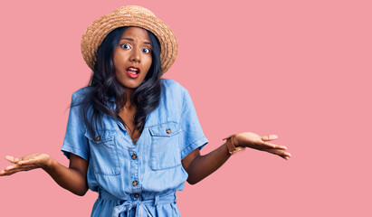 Young indian girl wearing summer hat clueless and confused with open arms, no idea concept.