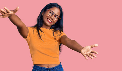 Young indian girl wearing casual clothes and glasses looking at the camera smiling with open arms for hug. cheerful expression embracing happiness.