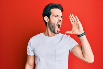 Young hispanic man wearing casual white tshirt shouting and screaming loud to side with hand on mouth. communication concept.