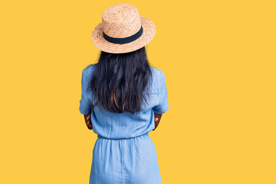 Young indian girl wearing summer hat standing backwards looking away with crossed arms