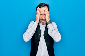 Middle age handsome man wearing elegant shirt and vest over isolated blue background with hand on head, headache because stress. Suffering migraine.