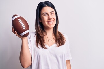 Young beautiful brunette woman playing rubgy holding football ball over white background looking positive and happy standing and smiling with a confident smile showing teeth