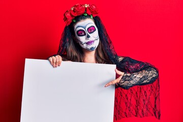 Young woman wearing day of the dead costume holding blank empty banner smiling happy pointing with hand and finger