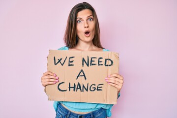 Beautiful caucasian woman holding we need a change banner scared and amazed with open mouth for surprise, disbelief face