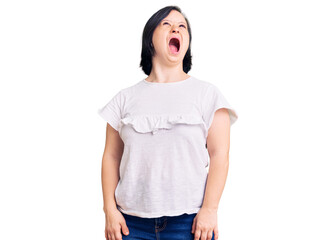 Brunette woman with down syndrome wearing casual white tshirt angry and mad screaming frustrated and furious, shouting with anger. rage and aggressive concept.
