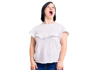 Fototapeta premium Brunette woman with down syndrome wearing casual white tshirt angry and mad screaming frustrated and furious, shouting with anger. rage and aggressive concept.