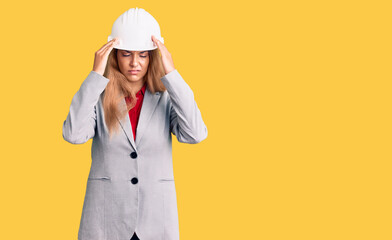 Beautiful young woman wearing architect hardhat with hand on head for pain in head because stress. suffering migraine.