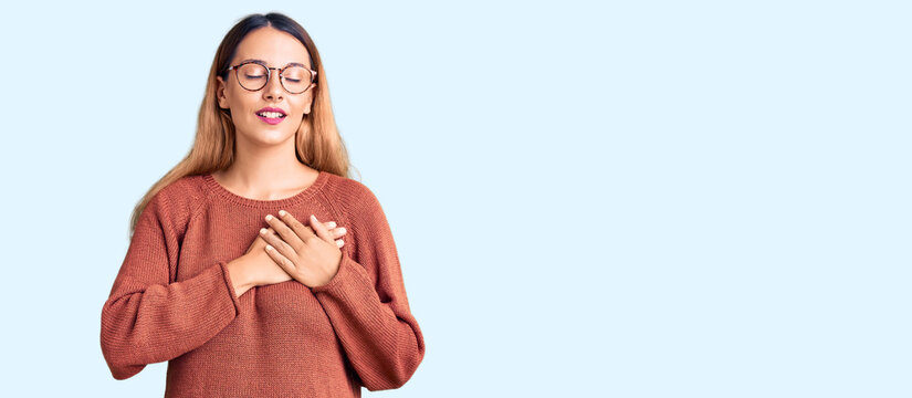 Beautiful young woman wearing casual clothes and glasses smiling with hands on chest with closed eyes and grateful gesture on face. health concept.