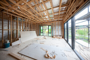 Interior view of a modern house undergoing construction, with timber frames, sliding glass doors...