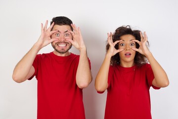 Young beautiful couple wearing red t-shirt on white background, keeping eyes opened to find a success opportunity.
