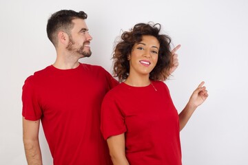 Obraz premium Smiling Young beautiful couple wearing red t-shirt on white background pointing up and looking at the camera