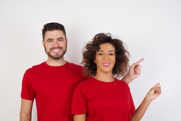  pretty Young beautiful couple wearing red t-shirt on white background looking indicating fingers hands side empty space advising novelt