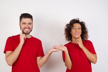 Funny Young beautiful couple wearing red t-shirt on white background hold open palm new product great proposition