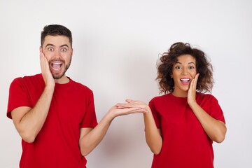 Crazy Young beautiful couple wearing red t-shirt on white background with an hairstyle advising discount prices hold open palm new product