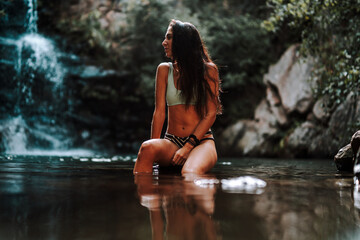 Chica joven atractiva en lago posando sobre una piedra