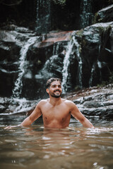 hombre bajo una cascada en plena naturaleza disfrutando de una ruta en su viaje de vacaciones