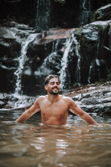 Fototapeta na wymiar hombre bajo una cascada en plena naturaleza disfrutando de una ruta en su viaje de vacaciones