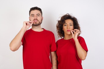 Young beautiful couple wearing red t-shirt on white background mouth and lips shut as zip with...