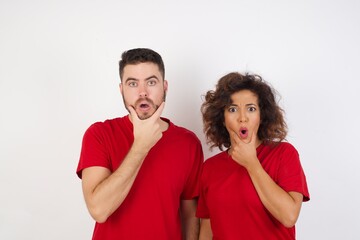Naklejka premium Young beautiful couple wearing red t-shirt on white background Looking fascinated with disbelief, surprise and amazed expression with hands on chin