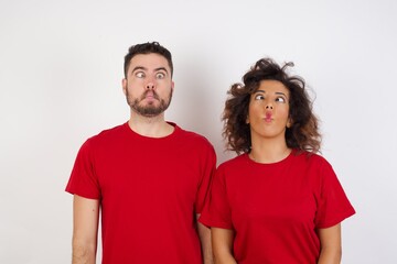 Young beautiful couple wearing red t-shirt on white background making fish face with lips, crazy and comical gesture. Funny expression.