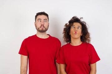Fototapeta premium Young beautiful couple wearing red t-shirt on white background making fish face with lips, crazy and comical gesture. Funny expression.