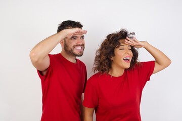 Young beautiful couple wearing red t-shirt on white background very happy and smiling looking far away with hand over head. Searching concept.