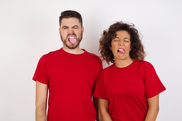 Fototapeta premium Young beautiful couple wearing red t-shirt on white background sticking tongue out happy with funny expression. Emotion concept.