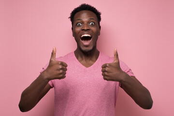 Handsome black man showing thumb up with cheerful attitude on pink background