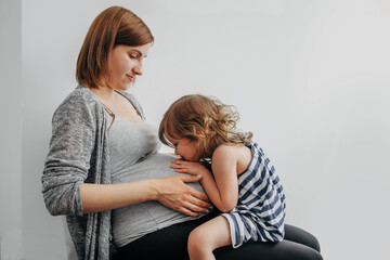 child girl sitting on the legs of a pregnant mother and communicating with the child in the woman's tummy