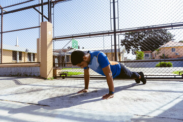 Athletic Hispanic young man doing push-ups with his arms outdoors on a sunny day, exercises with the body.