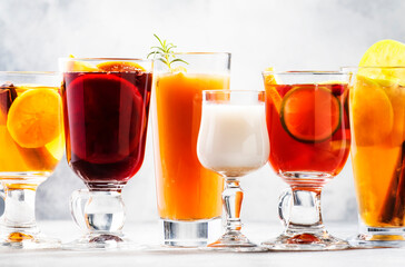 Selection of autumn or winter alcoholic hot drinks and cocktails - mulled wine, glogg, grog, eggnog, warm ginger ale, hot buttered rum, punch, mulled apple cider on gray background, copy space