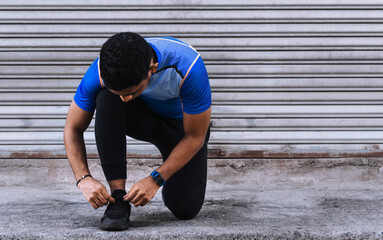 Athletic Hispanic young man tying his shoelaces to go for a run outdoors, copyspace