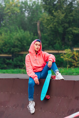 Young girl with short multicolored hair sits with skateboard in skatepark