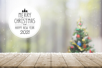 Christmas and Happy new year 2021 on empty wood table top on blur bokeh Christmas tree background with snowfall - can be used for display or montage your products.