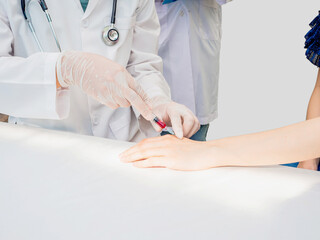  closeup hands of doctor in uniform wear stethoscope use syringe to patient&rsquo;s hands do blood test with trainee standing beside and taking note. white copy-space, healthcare medical care concept