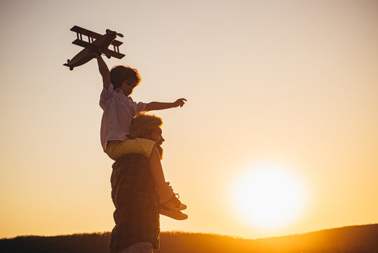 Sunset silhouette of Happy father and child son with airplane dreams of traveling. Father carrying his son on shoulders.