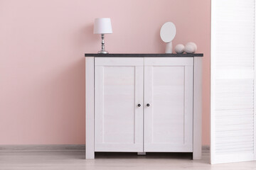Modern chest of drawers with lamp and mirror near color wall in room