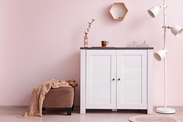 Modern chest of drawers with lamp and ottoman near color wall in room