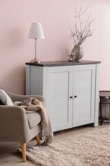 Modern chest of drawers with lamp and armchair near color wall in room